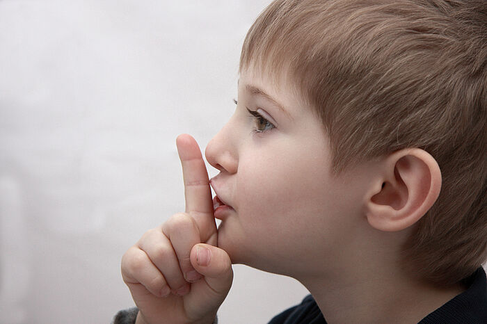 Profilaufnahme eines kleinen Jungen der seinen Zeigefinger an seinen Mund drückt