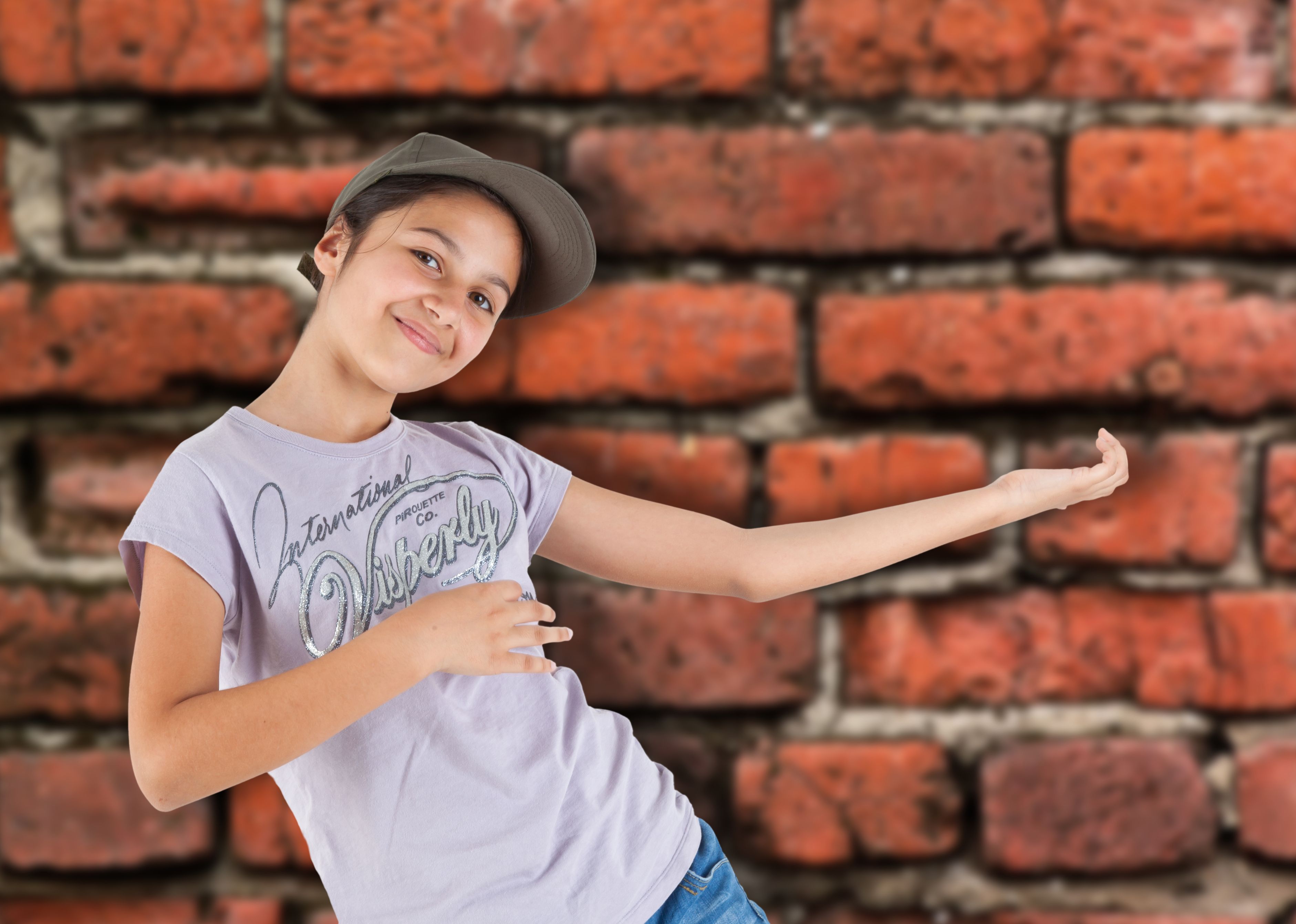 ein Mädchen im Hiphop-Outfit tanzt vor einer Backsteinmauer