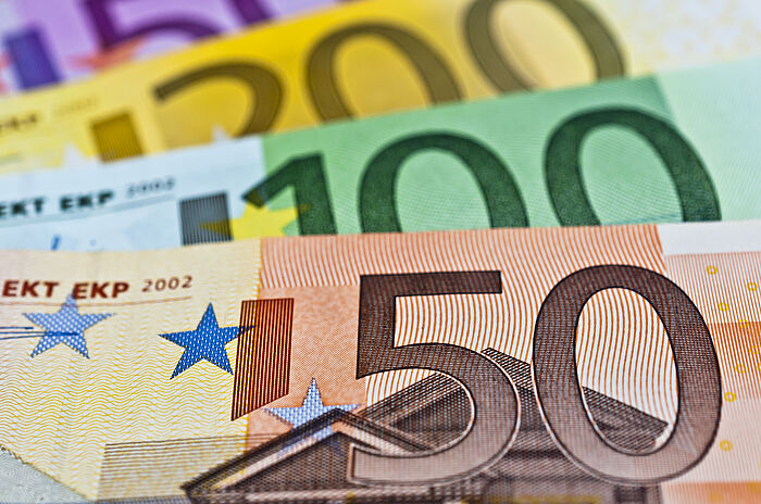 Zu sehen sind vier Eurogeldscheine. Diese sind hintereinander gefächert  angeordnet. Der vorderste Geldschein ist der braune 50 Euroschein. Dahinter ist die obere Hälfte des grünen 100 Euroscheins zu sehen. Dahinter ist die obere Hälfte des gelben 200 Euroscheins zu sehen. Dahinter ist noch ein kleines Stück des oberen Teils des magentafarbenden 500 Euroscheins zu sehen.
