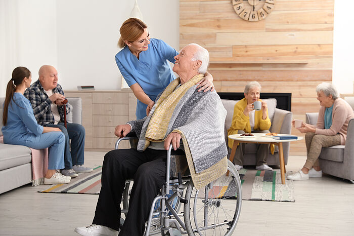 Pflegekraft legt Mann im Rollstuhl Decke über die Schulter