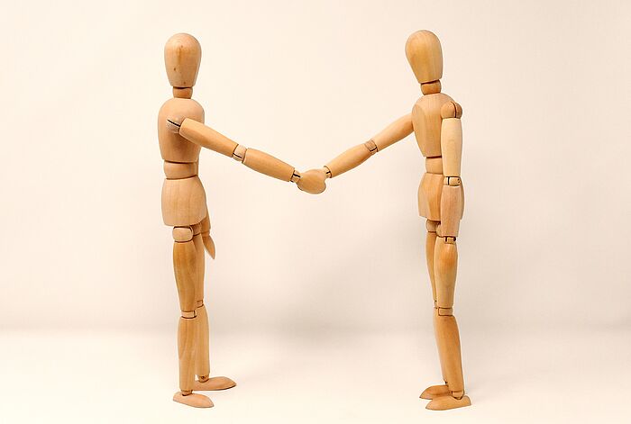Zwei Holzfiguren reichen sich in einem symbolischen Akt die Hand, was für Zusammenarbeit steht