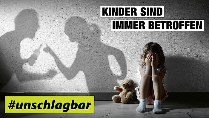Ein Kind sitzt auf dem Boden, daneben liegt ein Teddybär, als Schatten zu sehen, wie sich zwei Erwachsene streiten