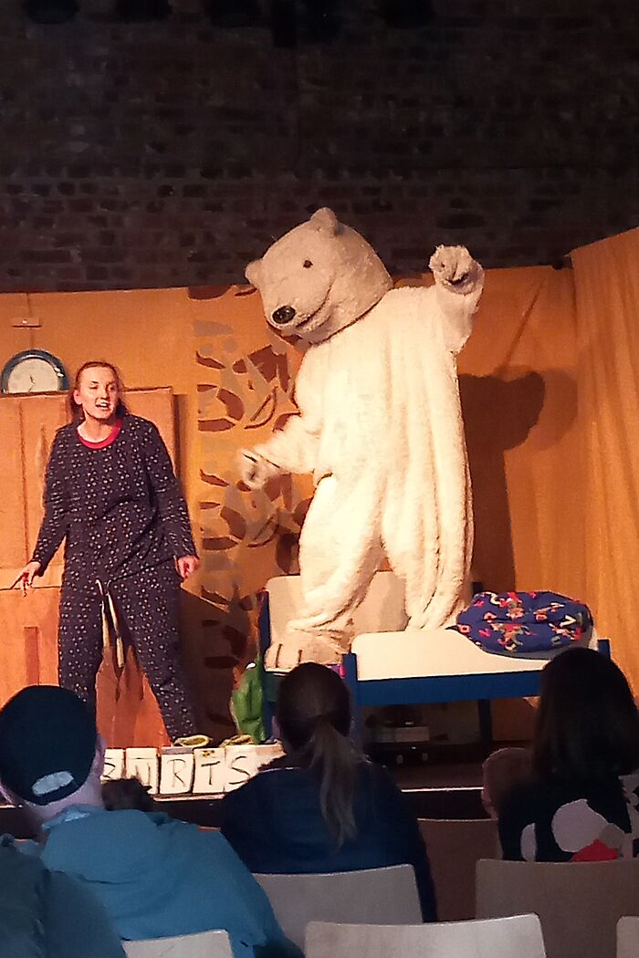 Eine Schauspielerin im Schlafanzug neben einer Person im Bärenkostüm.