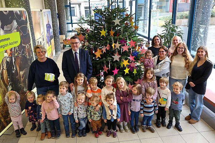 Mehrere Kinder und Erwachsene vor einem Weihnachtsbaum.