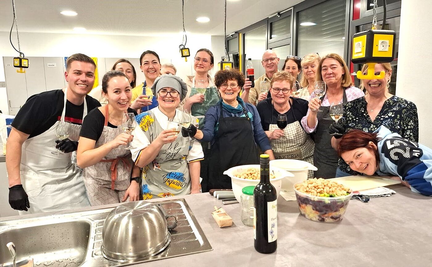 Mehrere Menschen mit Kochschürzen lachen in die Kamera.