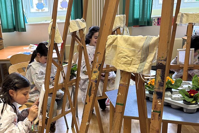 Kinder malen an Staffeleien mit Acrylfarbe Primeln auf Leinwände.
