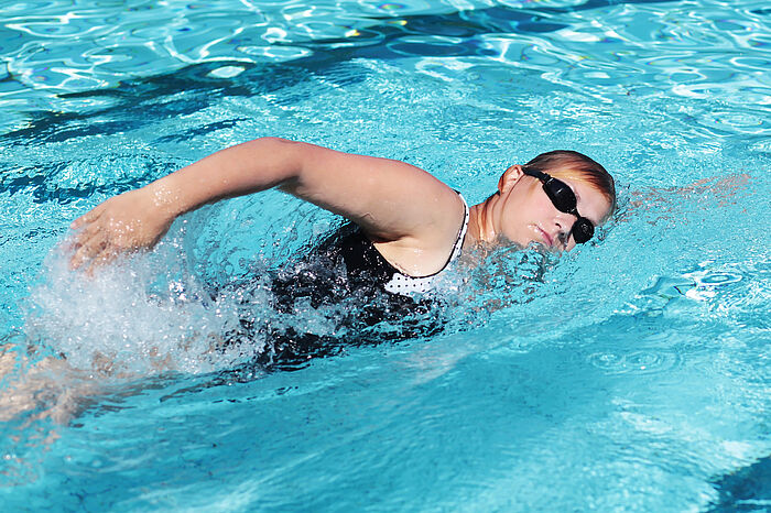 Frau mit Schwimmbrille schwimmt sportlich in einem Schwimmbecken