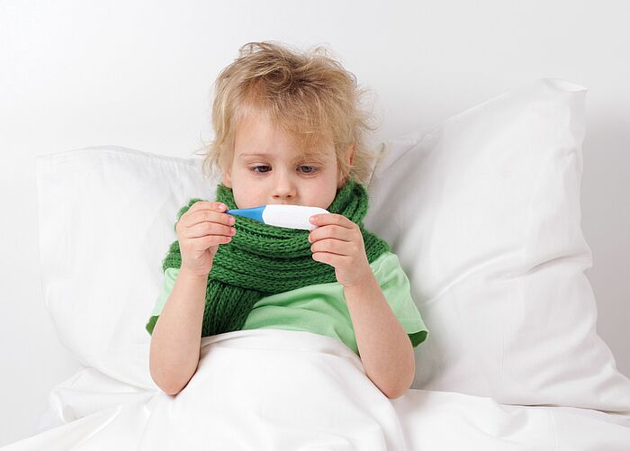 kleiner Junge sitzt im Bett und betrachtet Fieberthermometer