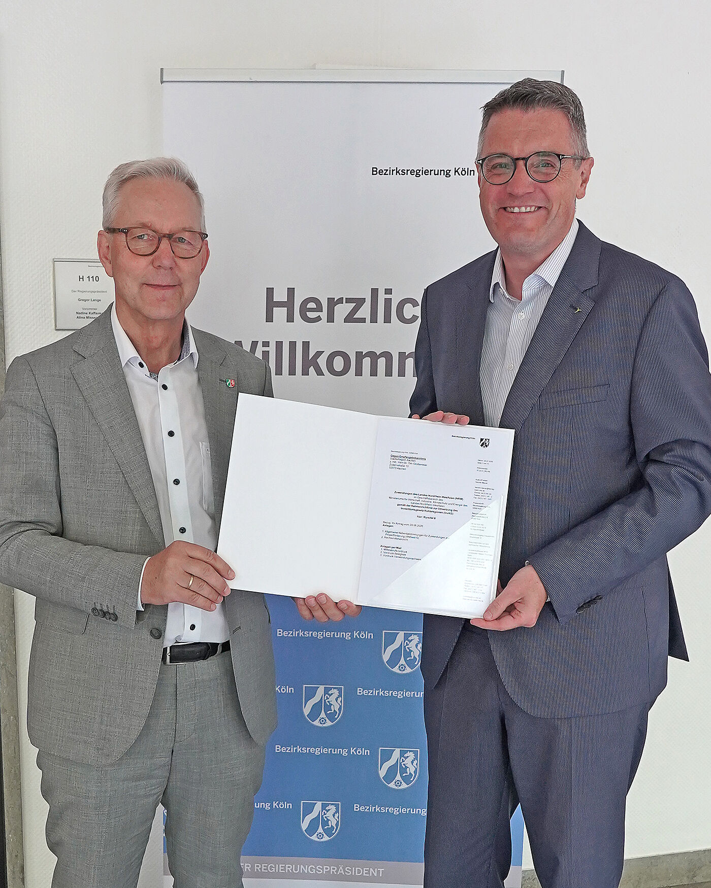 Regierungspräsident Gregor Lange (l.) übergibt den Förderbescheid über fast eine Million Euro an Städteregionsrat Dr. Tim Grüttemeier.