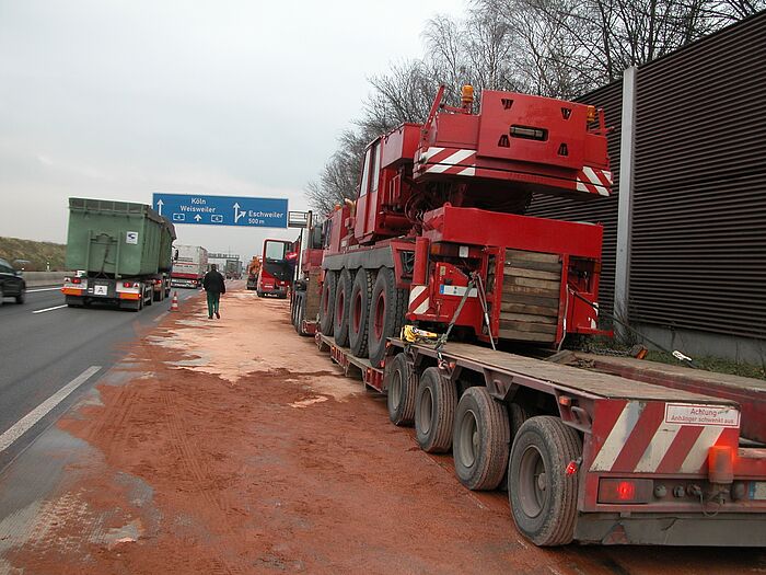 Ölunfall vor der Ausfahrt Eschweiler, am Standstreifen ist ein Schwertransporter zu sehen und ein abgestreuter Bereich mit rotem Sand und Stau auf der Autobahn.