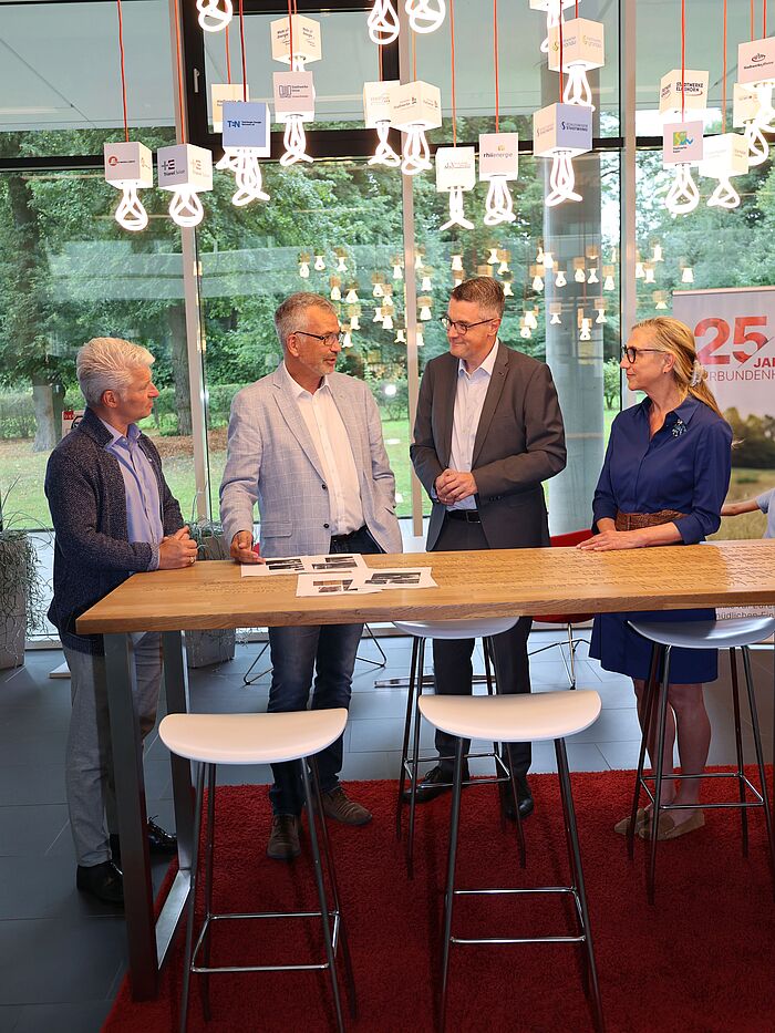 Vier Erwachsene an einem Tisch. Auf dem Tisch liegen Fotos.