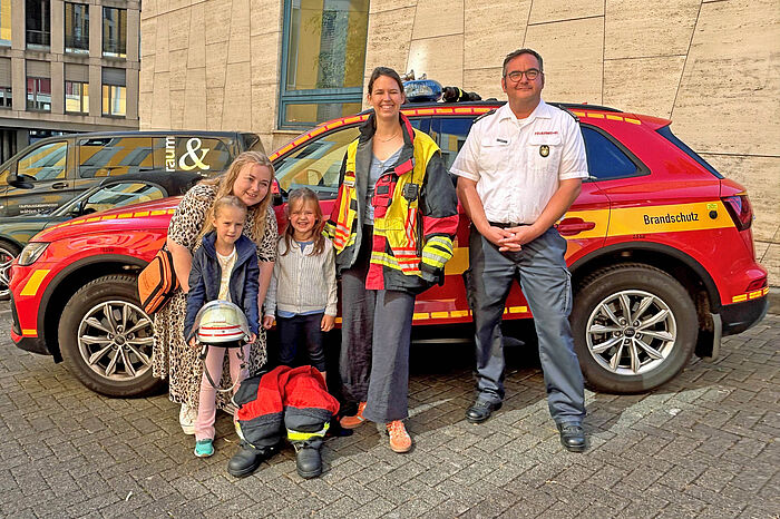 Zwei Mädchen, zwei Frauen und ein Feuerwehrmann vor einem kleinen Einsatzwagen.
