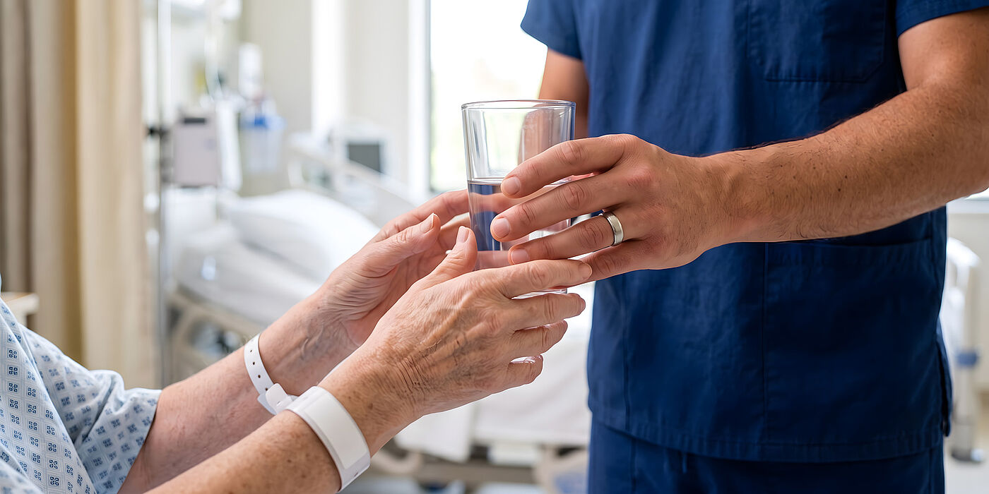 Krankenpfleger reicht Patientin ein Wasserglas
