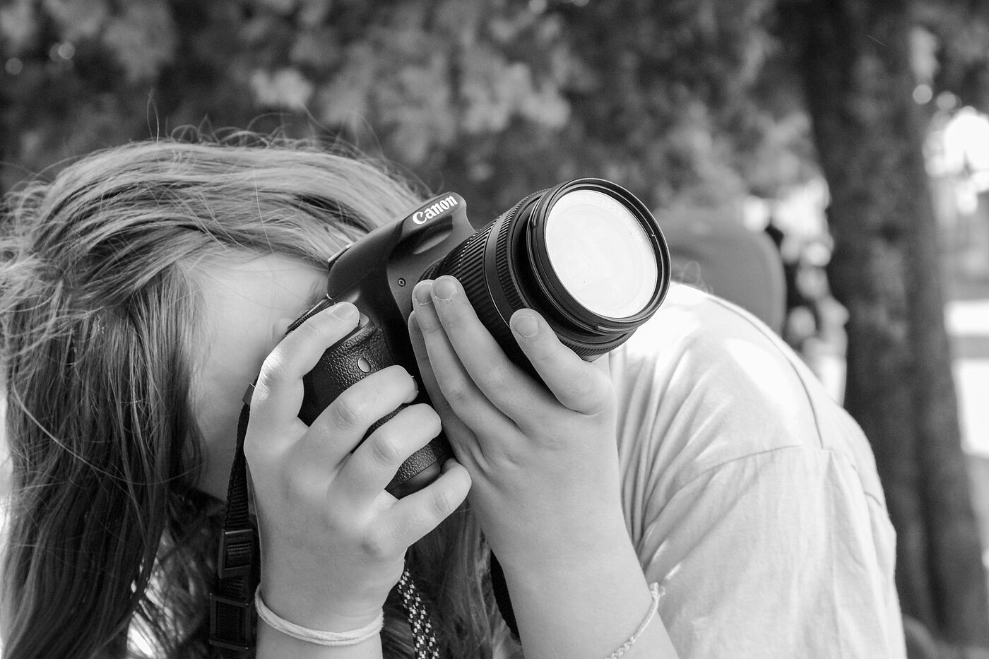 Eine jugendliche Person hält eine Spiegelreflexkamera in der Hand und schaut durch den Sucher