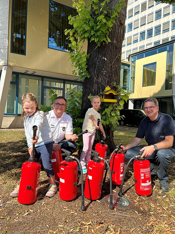 Zwei Mädchen und zwei Männer mit Feuerlöschern vor einem Baum.