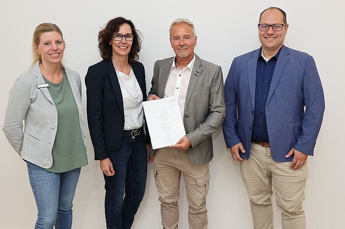 Drei Männer und eine Frau. Ein Mann hält eine Urkunde in der Hand.