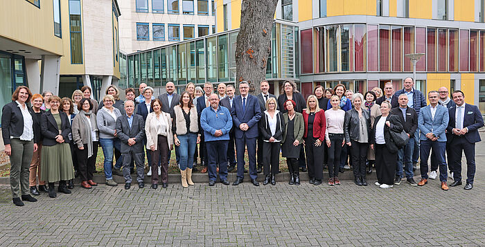 Viele Menschen auf einem Gruppenbild vor einem gelben Gebäude.