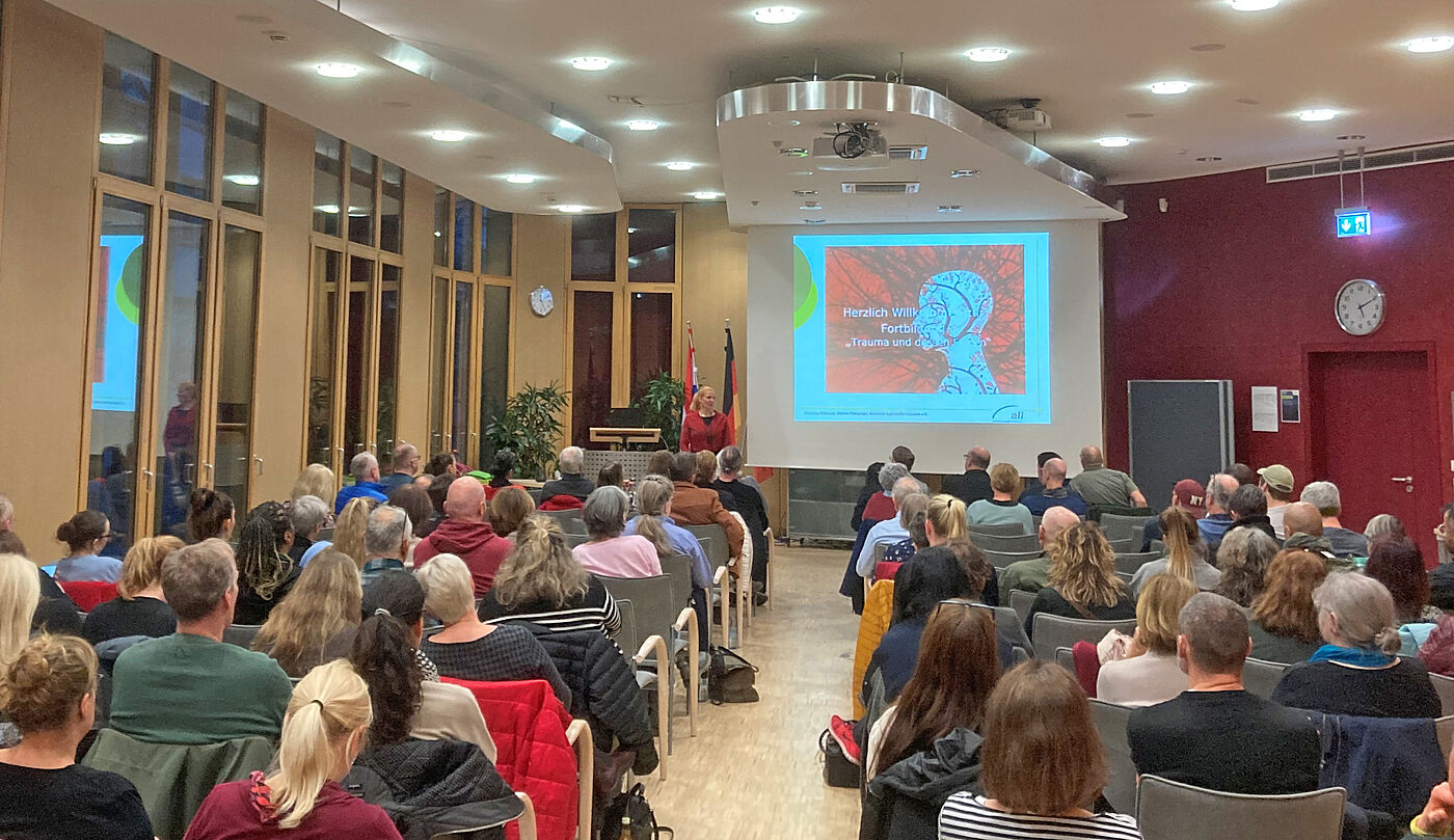 Mehrere Menschen sitzen in einem Saal vor einer Leinwand