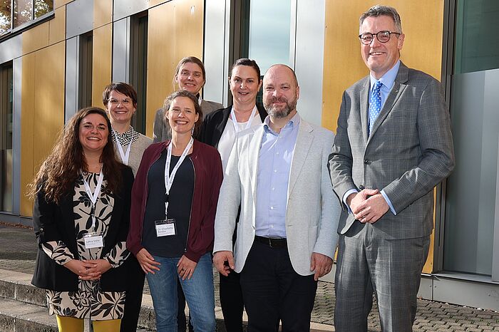 Mehrere Männer und Frauen stehen vor einem gelben Gebäude.