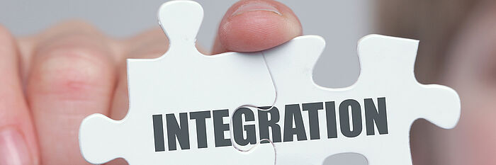 Zwei Puzzleteile in einer Hand, die das Wort "Integration" ergeben