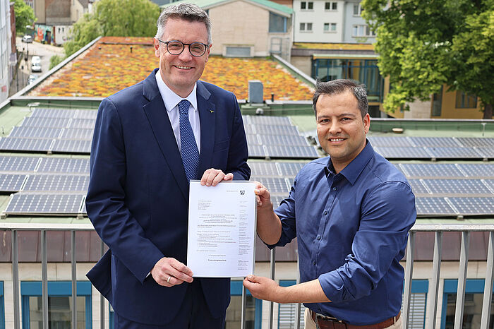 Zwei Männer auf einem Dach halten eine Urkunde in der Hand.
