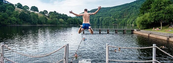 Freibad Eifel Freibad, Mann springt von einem Steg ins Wasser.