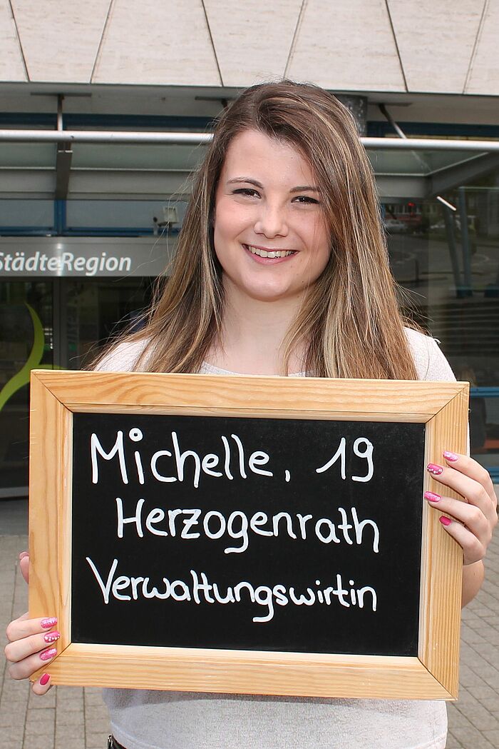Michelle Ward hält Tafel mit ihrem Namen, ihrem Alter und ihrem Ausbildungsberuf