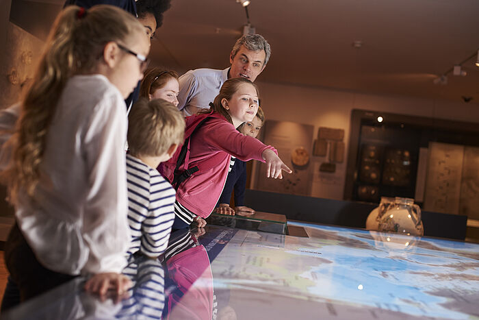 Kinder im Museum zeigen auf eine visualisierte Tafel