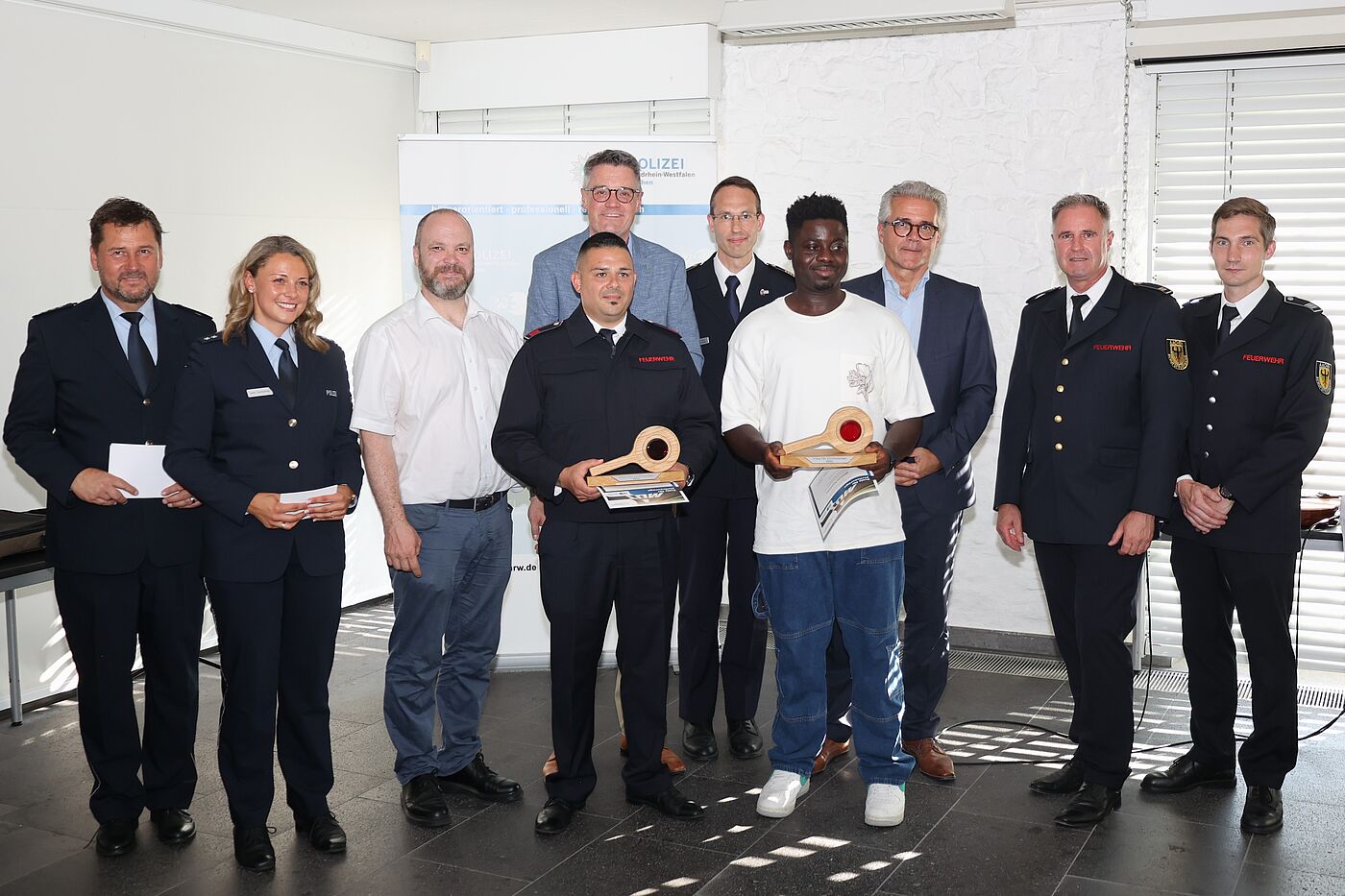 Mehrere Menschens tehen nebeneinander. Auch Polizisten sind dabei. Zwei Personen halten einen Preis.