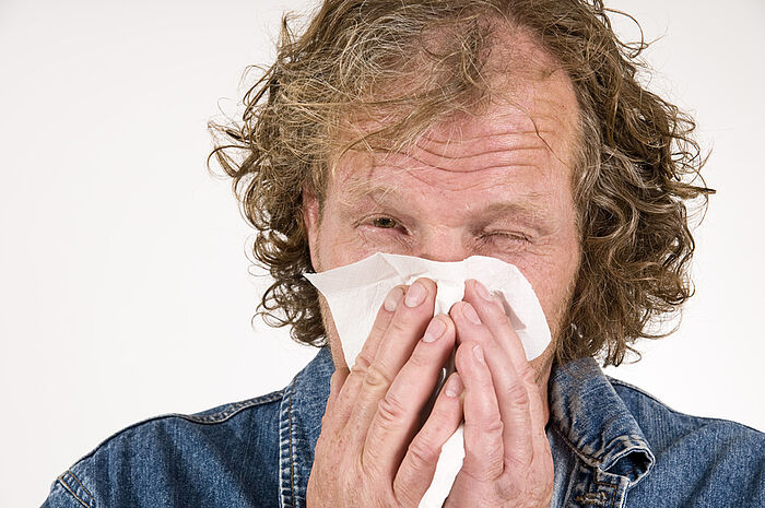 Mann putzt sich mit einem Taschentuch die Nase