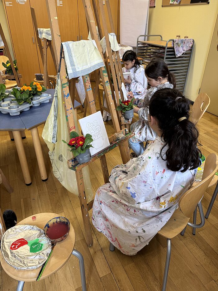 Kinder malen an Staffeleien Primeln mit Acrylfarbe auf Leinwände.