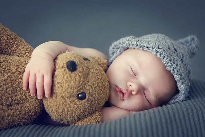 Ein Baby schläft mit einem Teddy im Arm