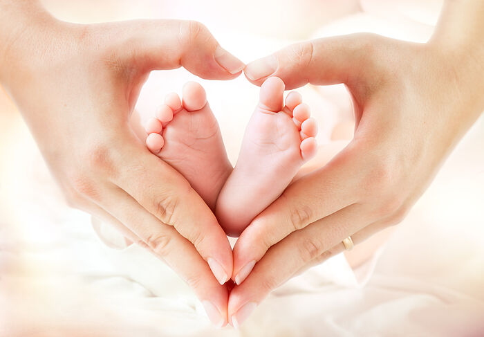 Kindergesundheit/ Frühe Hilfen Babyfüße werden von einer Frauenhänden Herzhaltung gehalten