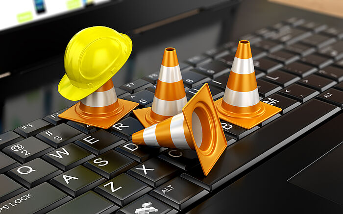 Tastatur eines Laptops mit kleinen Absperrkegeln und einem kleinen Bauhelm
