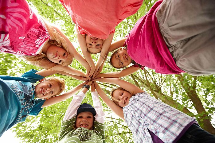 6 Kinder stehen im Kreis und bilden mit ihren gestreckten Armen einen Dach 