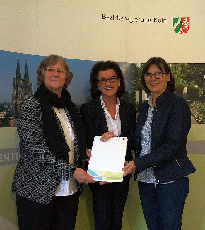Drei Frauen stehen nebeneinander und halten gemeinsam den Förderbescheid