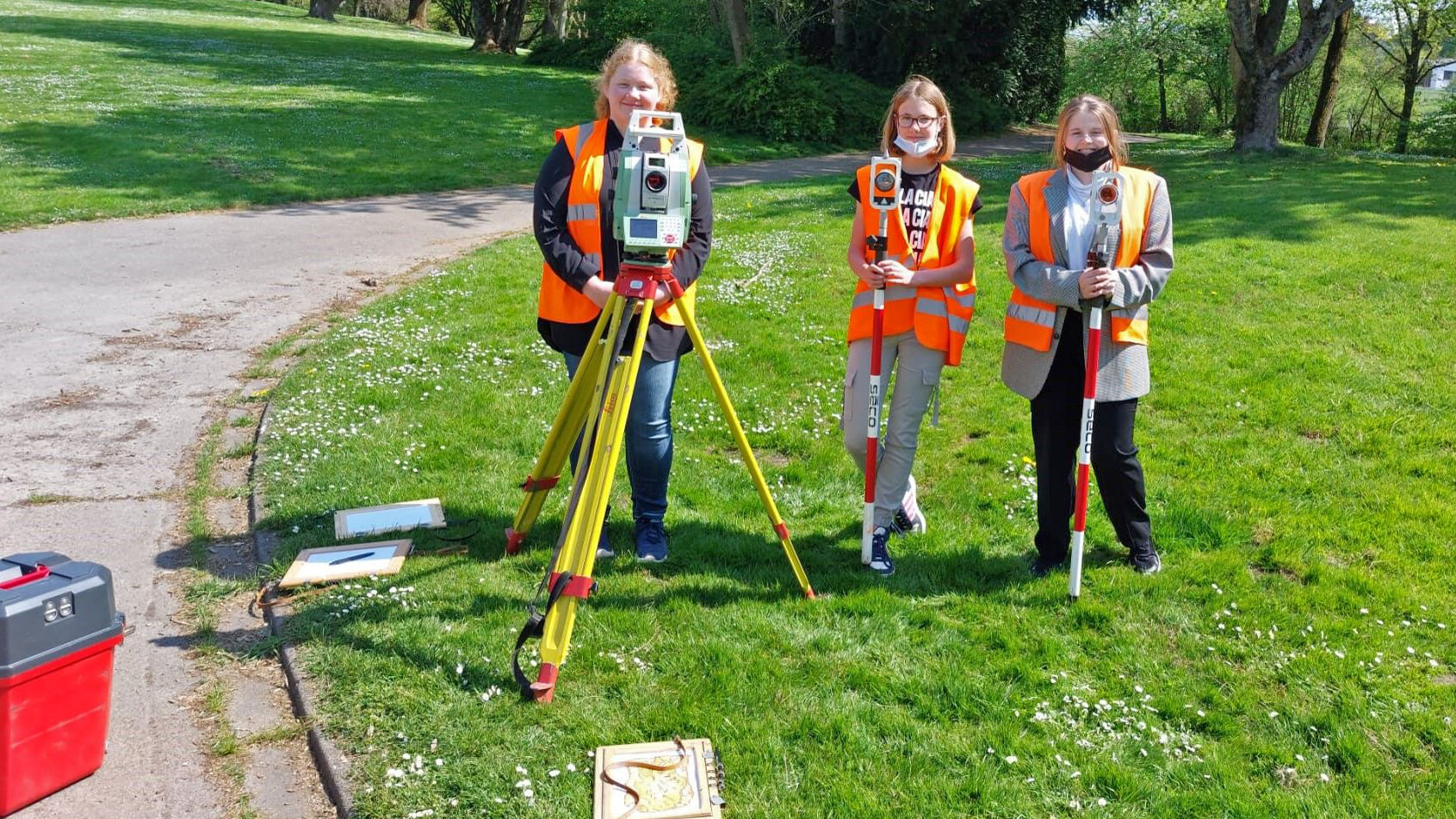 Drei Praktikantinnen beim Girls Day sind mit Vermessungsmaterial in einem Parkk unterwegs.