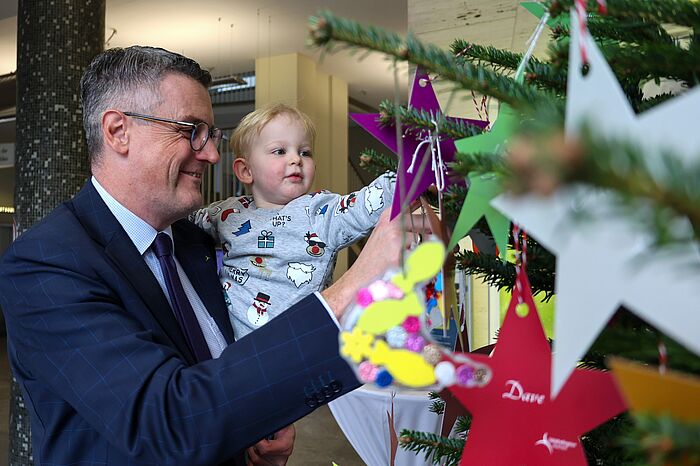 Ein Mann mit einem Jungen auf dem Arm. Sie schmücken einen Weihnachtsbaum.
