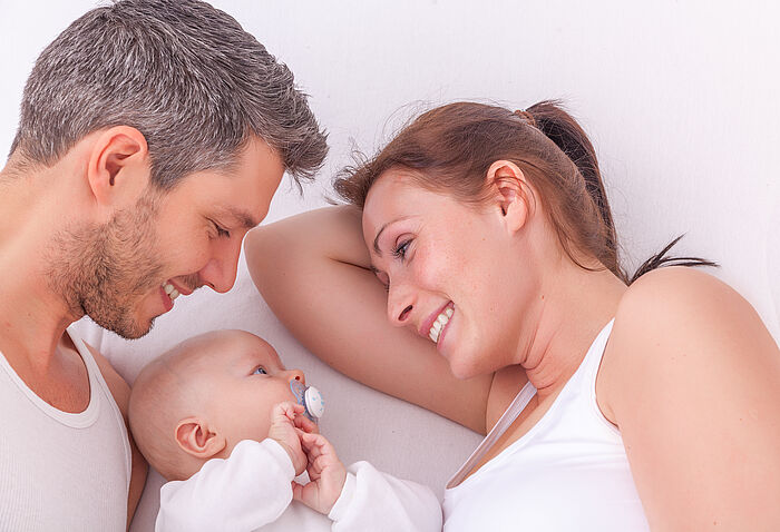 Mutter und Vater betrachten lachend ihr zwischen ihnen beiden liegendes Baby