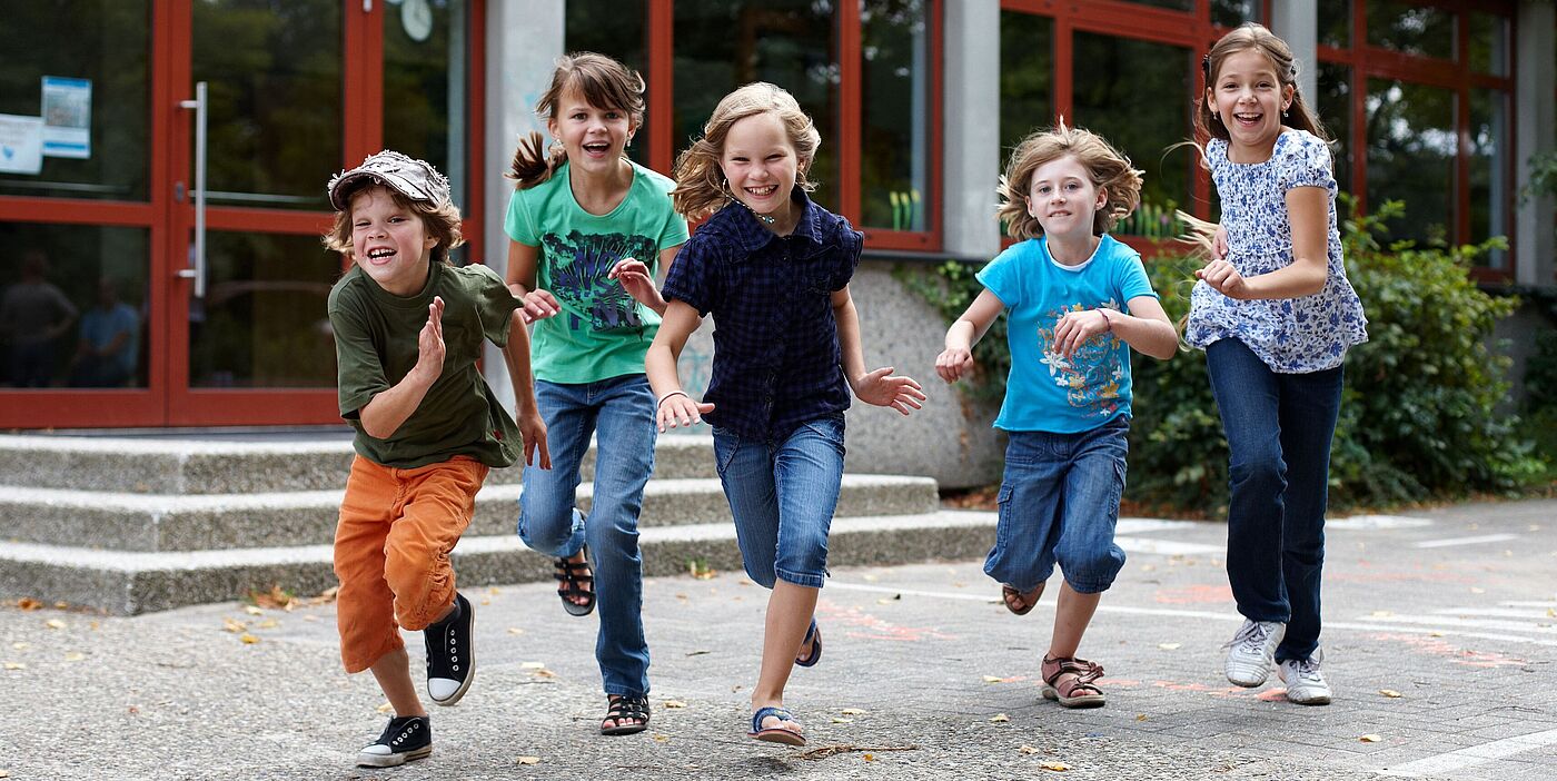 Fünf Kinder rennen über einen Schulhof und lachen