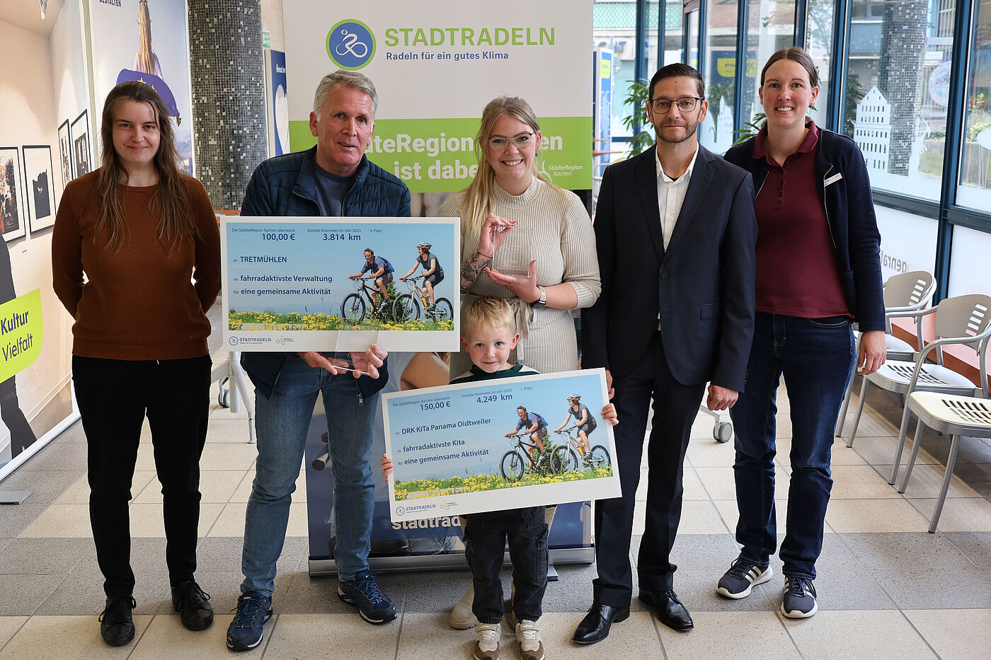 Drei Frauen, zwei Männer und ein Kind mit großen Schecks in der Hand.