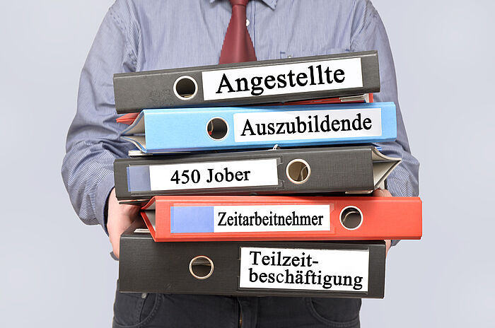 Mann trägt verschiedene Aktenordner, die beschriftet sind mit: Angestellte, Auszubildende, 450 Jober, Zeitarbeitnehmer,Teilzeitbeschäftigung
