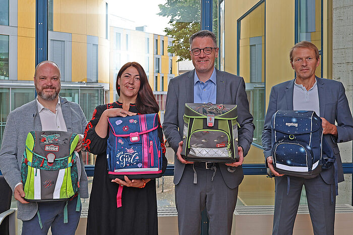 Drei Männer und eine Frau mit Schulranzen in der Hand.