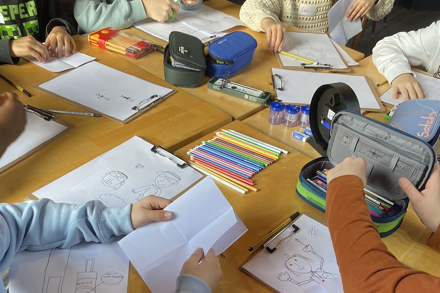 Kinderhände mit Stiften und Malpapier.