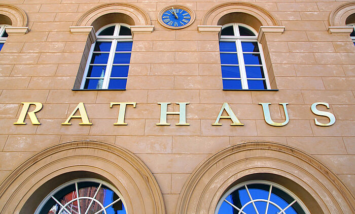 Zu sehen ist ein Teil der Fassade eines Rathauses. Auf der Fassade steht das Wort "Rathaus".