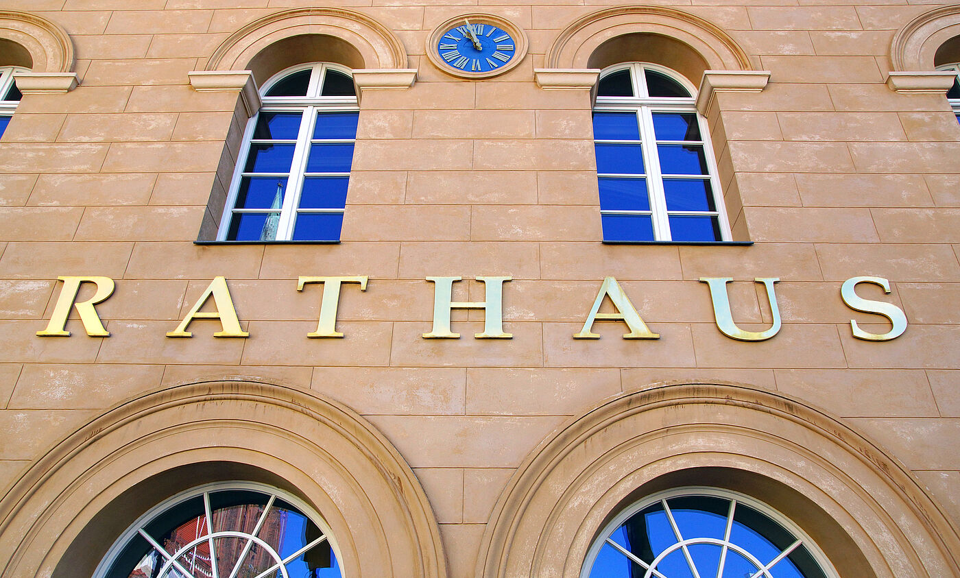 Zu sehen ist ein Teil der Fassade eines Rathauses. Auf der Fassade steht das Wort "Rathaus".