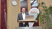 Eine männliche Person steht hinter einem Rednerpult, im Hintergrund ist ein Aufsteller mit dem Logo von render zu sehen und eine Uhr