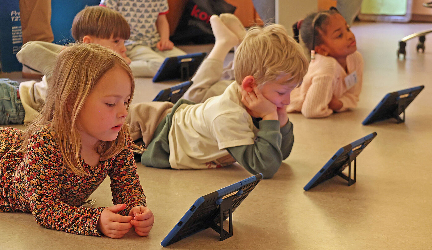 Drei Kinder vor Tablets auf dem Boden.