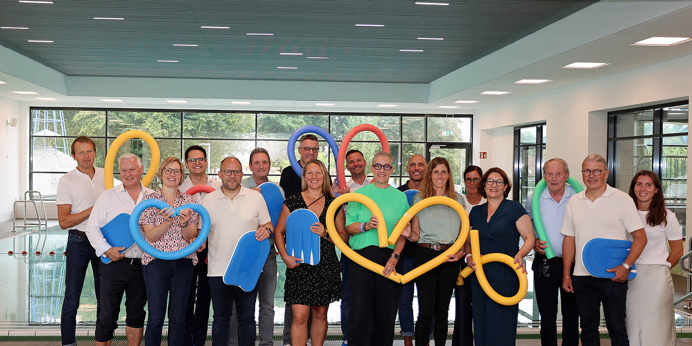 Viele Menschen in einem Schwimmbad mit Poolnudeln und Schwimmbrettern in der Hand.
