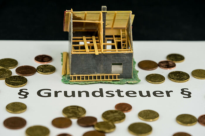 Modell eines Hauses mit Geldstücken drumherum und dem Schriftzug Grundsteuer